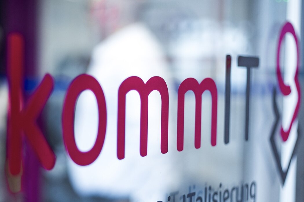 Foto des kommIT-Logos auf einer Glastür im kommIT-Büro